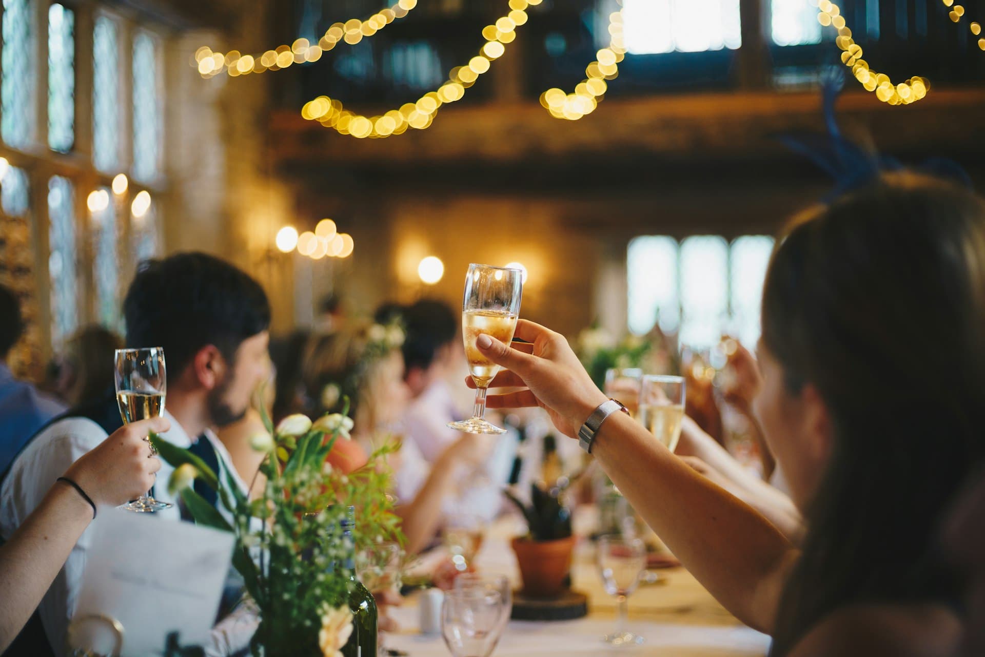 Gäster lyfter champagneglas till en skål under en bröllopsmiddag med varma lampor i bakgrunden.